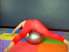 רג'ינה נואר, אישה בוגרת, מתרגלת יוגה בחדר כושר כשהיא לובשת בגד גוף אדום, גרביוני יוגה ומגולחת