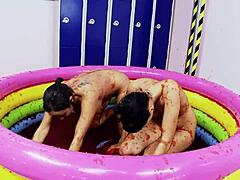 Lesbiska med stora falska bröst njuter av att brottas i en pool med gelé