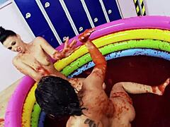 Lesbiska med stora falska bröst njuter av att brottas i en pool med gelé